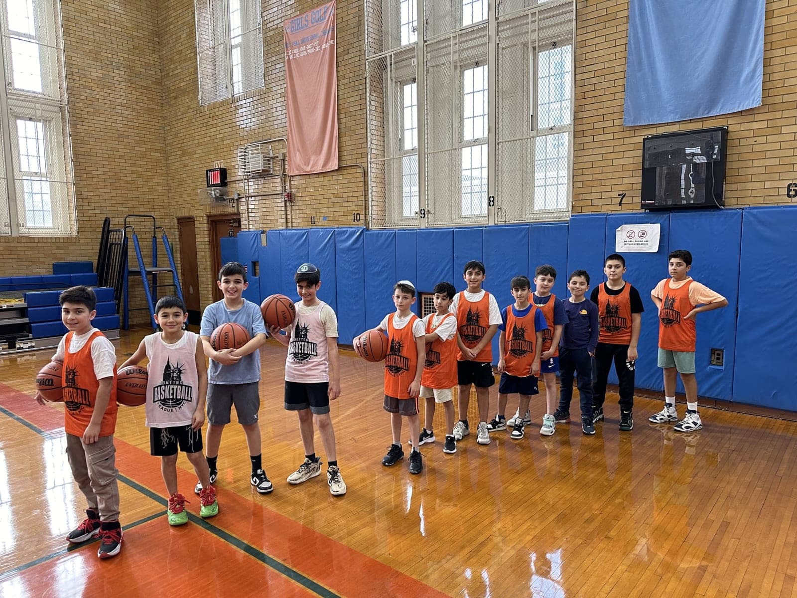 A line of players in BBLNYC pinnies standing across the gym floor, several holding basketballs