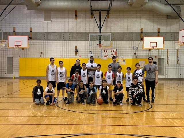 A group of players and coaches posed for a team photo, a basketball set on the floor in front
