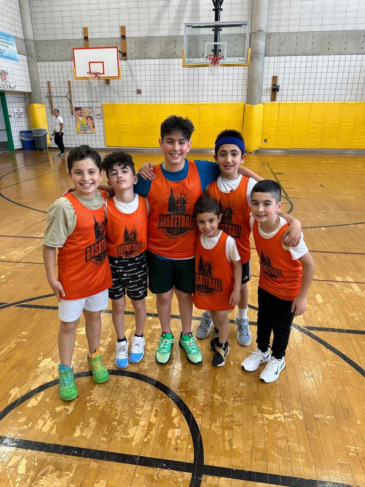 Six BBL NYC players in orange pinnies, arms around each other's shoulders, posed under the hoop after a Sunday session