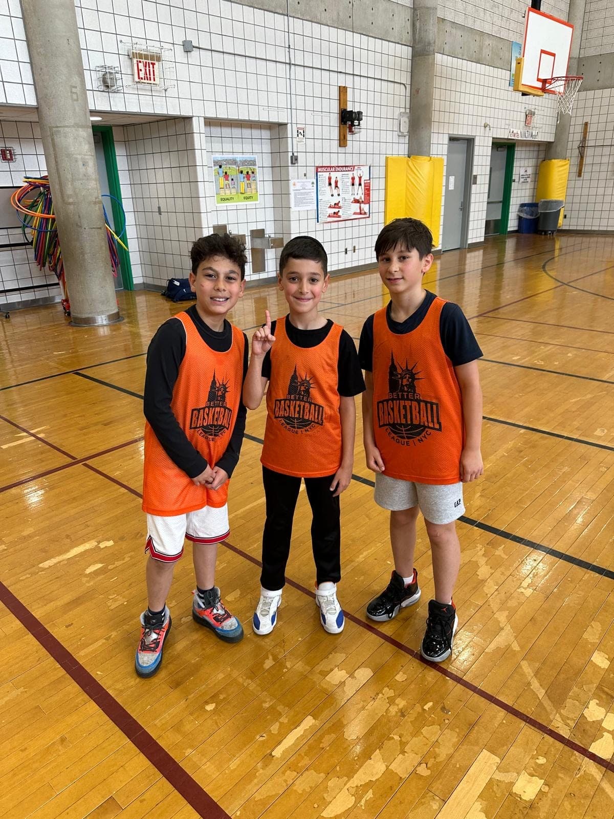 Three players in orange BBL NYC pinnies standing together at the side of the gym